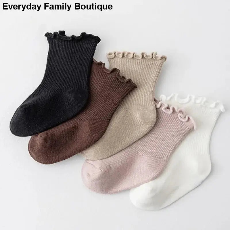 Five pairs of ruffled cotton socks in neutral colors including black, brown, beige, pink, and white.