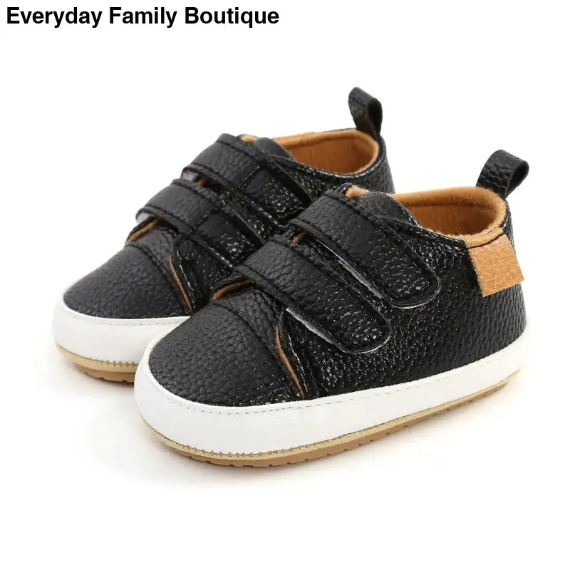 Black leather baby shoes with velcro straps and white soles.