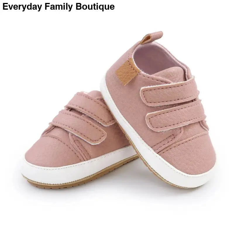 Pink velcro baby sneakers with white soles and gold accents.