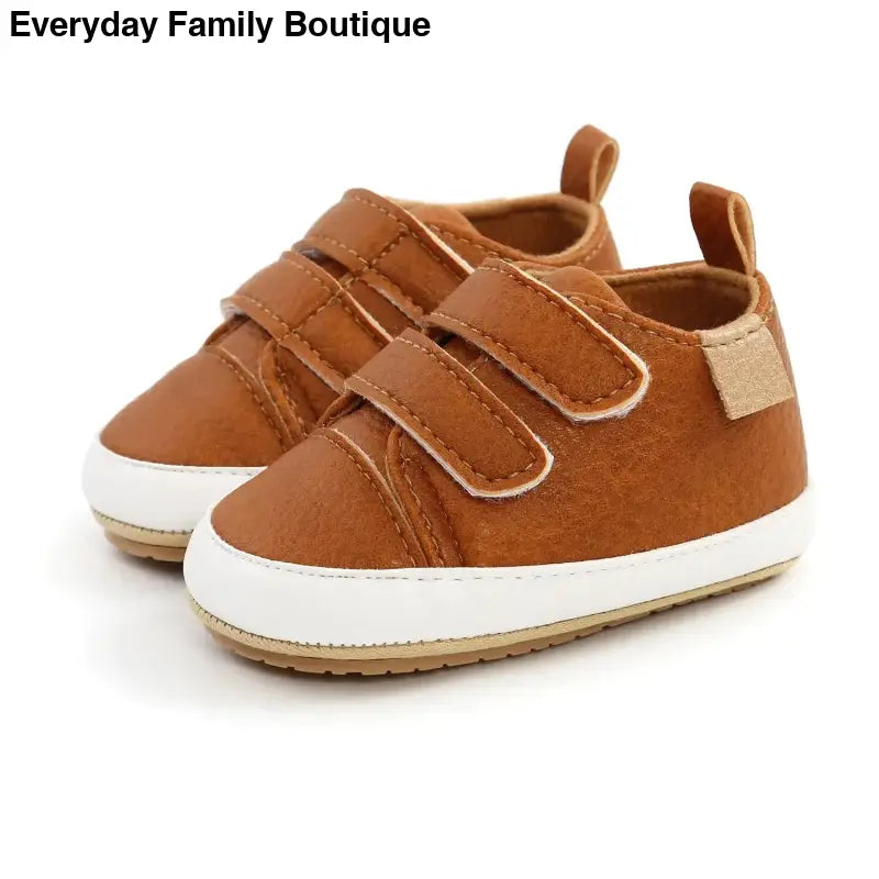 Brown leather baby shoes with velcro straps and white soles.