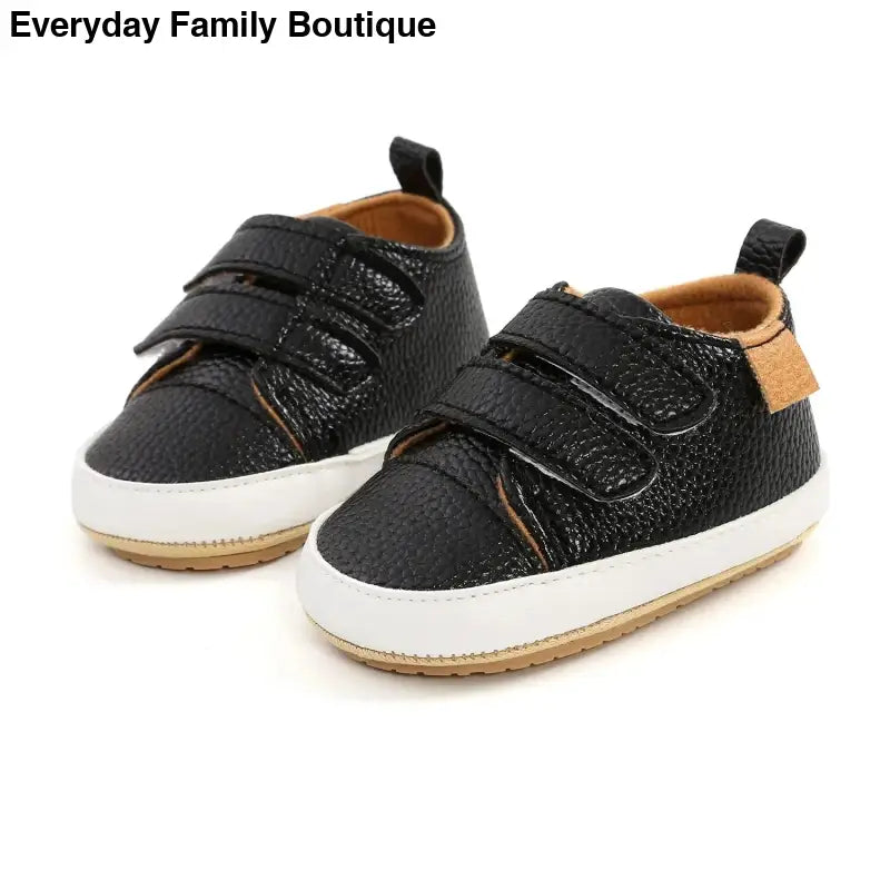 Black leather baby shoes with velcro straps and white soles.