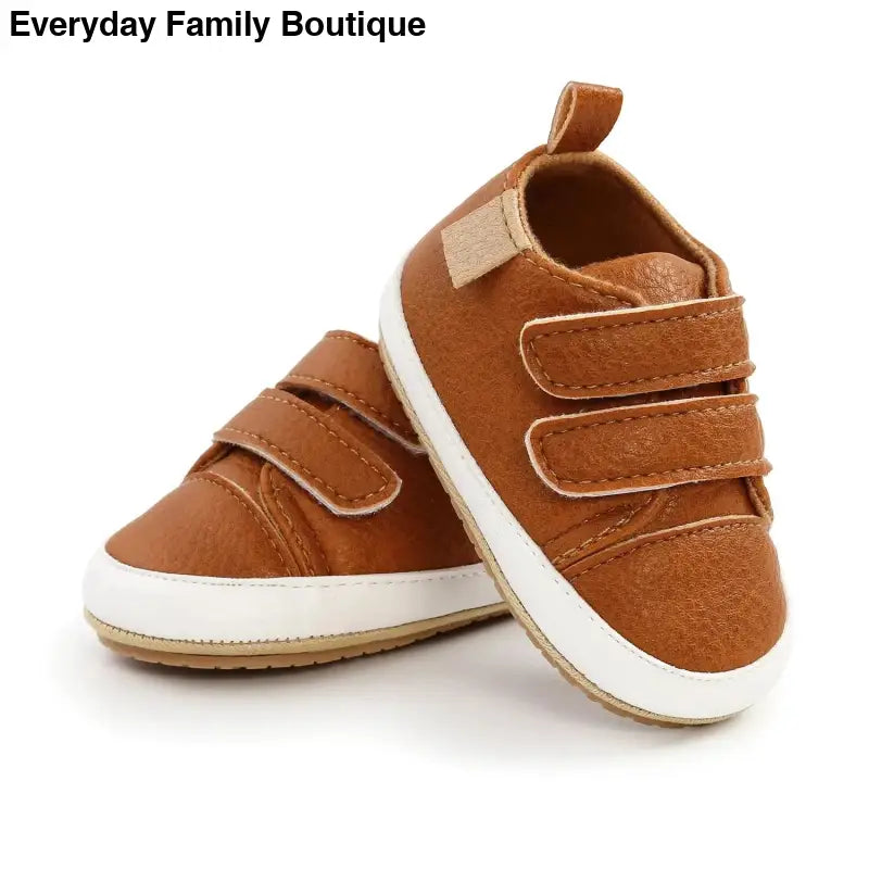 Brown suede baby shoes with velcro straps and white soles.