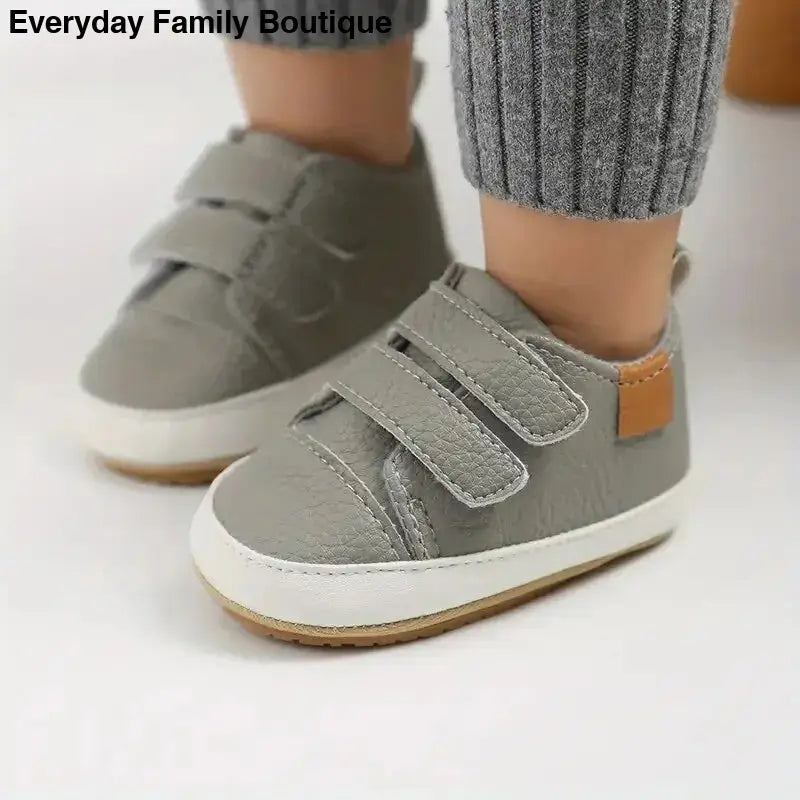 Gray velcro baby sneakers with white soles and brown accents.