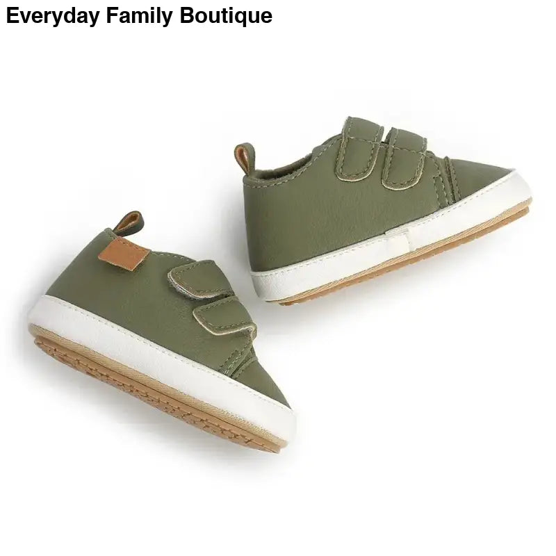 Pair of olive green baby sneakers with velcro straps and brown leather tabs.