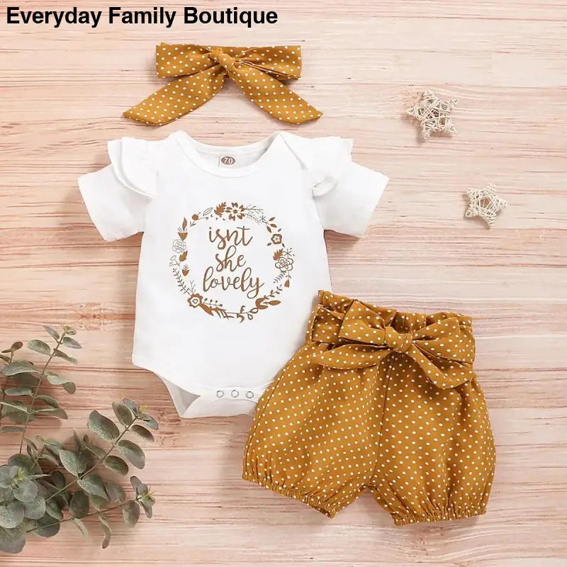 Baby outfit set featuring a white onesie with floral wreath design, mustard polka dot shorts, and matching bow headband.