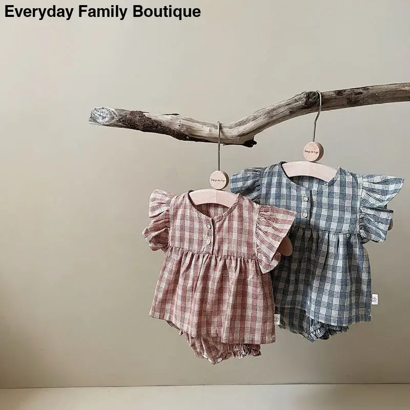 Two plaid baby rompers hanging from a tree branch.