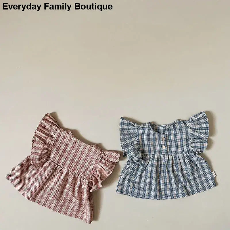 Two gingham patterned baby tops with ruffled sleeves in pink and blue.