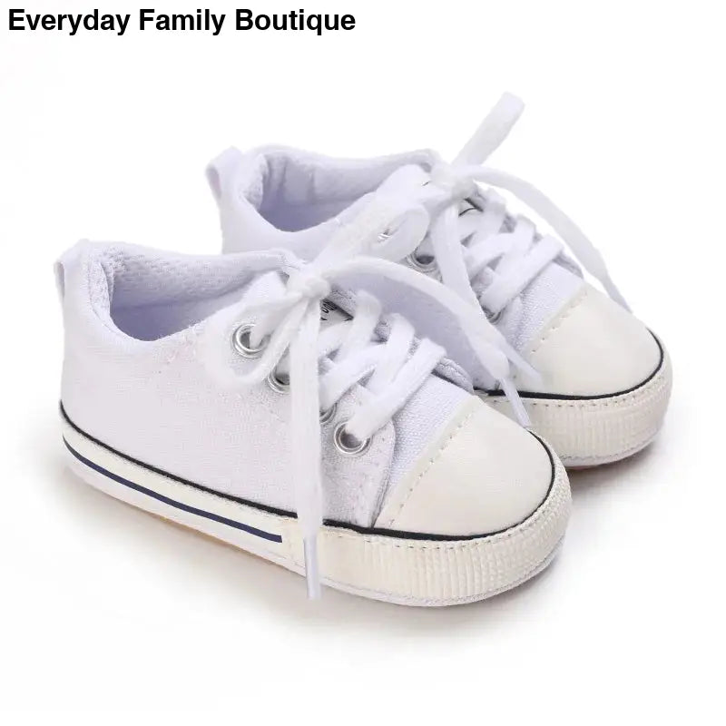 White canvas baby sneakers with laces and rubber toe caps.