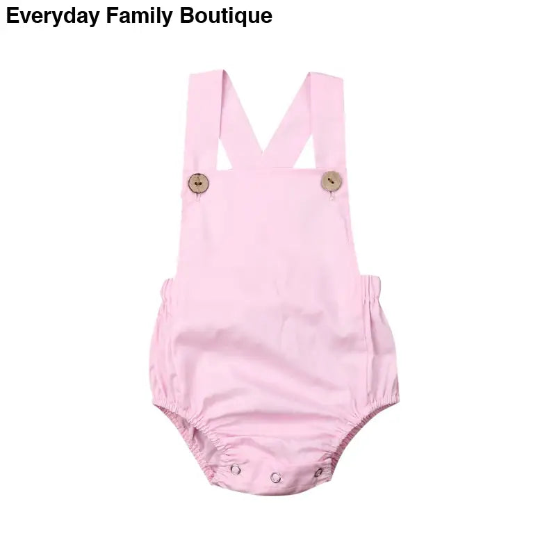 Pink cotton baby romper with cross-back straps and button closures.