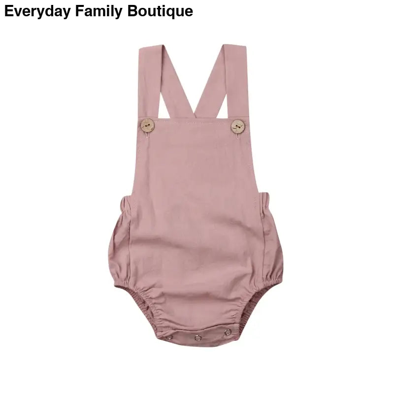 Pink baby romper with cross-back straps and button details.