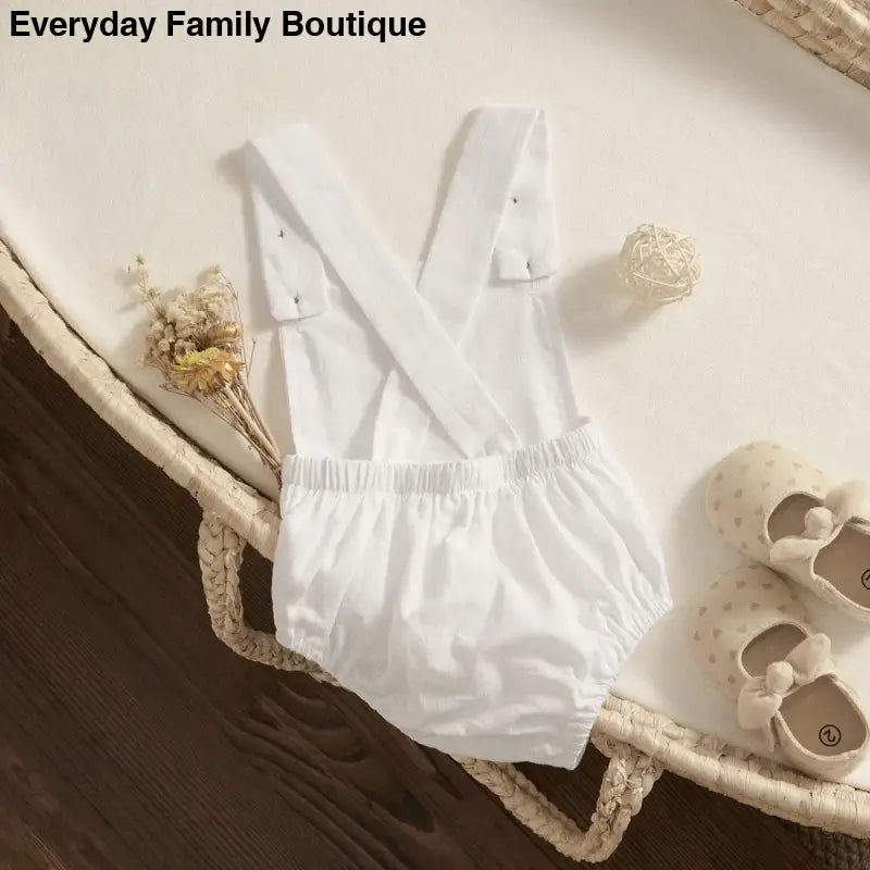 White cotton baby romper with crossed suspender straps.