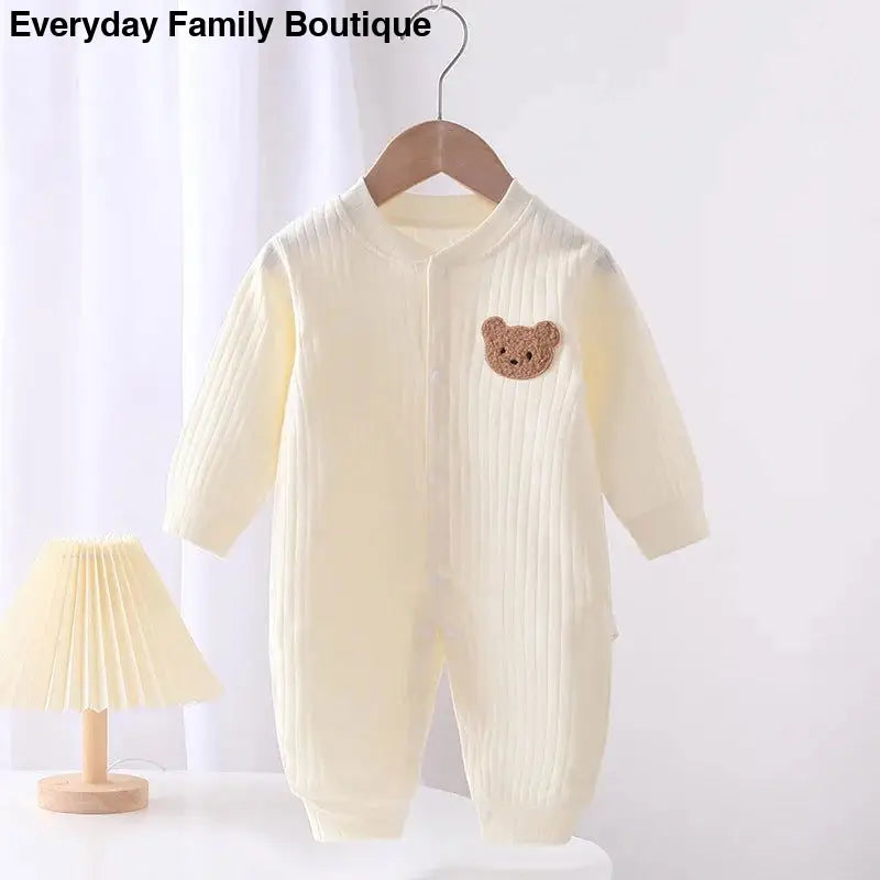 Cream-colored knit baby romper with a brown teddy bear patch.