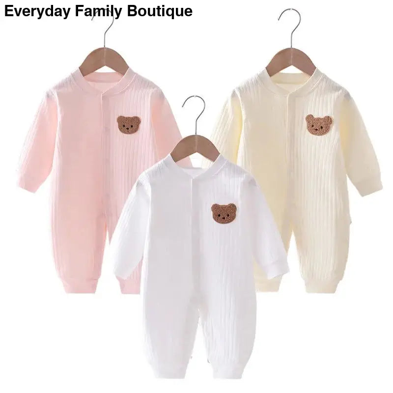 Three baby onesies with teddy bear patches in pink, white, and cream colors.