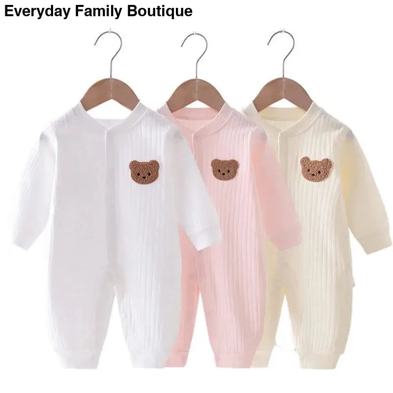 Three baby onesies with teddy bear patches in white, pink, and cream colors.