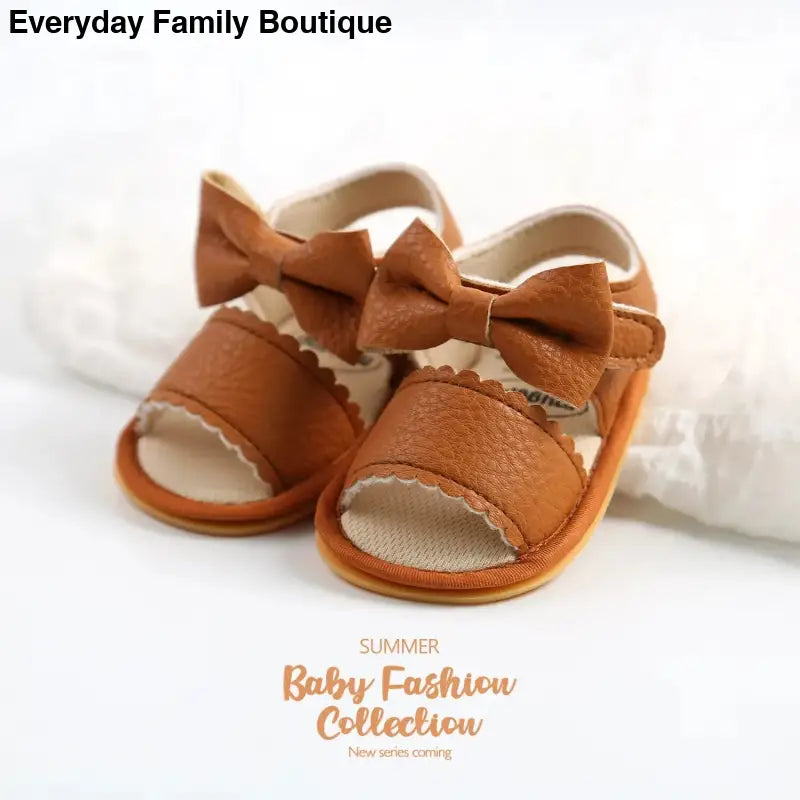 Brown leather baby sandals with decorative bows on top.