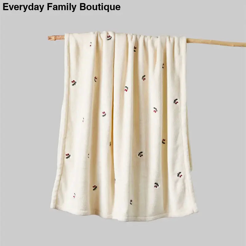 Cream-colored blanket with small scattered floral designs hanging on a wooden rod.