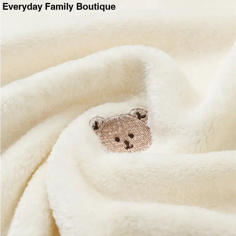 Cute embroidered teddy bear face on cream-colored fabric.