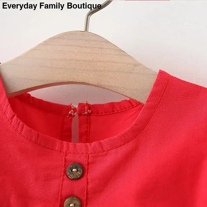 Red garment with decorative buttons hanging on a wooden hanger.