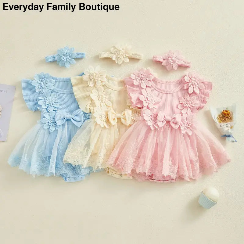 Three delicate tulle dresses with floral appliques in blue, cream, and pink, each with matching headbands.