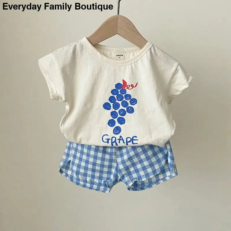 White t-shirt with blue grape design paired with blue gingham shorts.