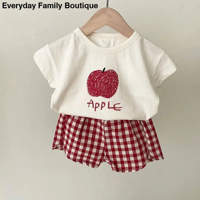 White t-shirt with red glitter apple design paired with red gingham shorts.