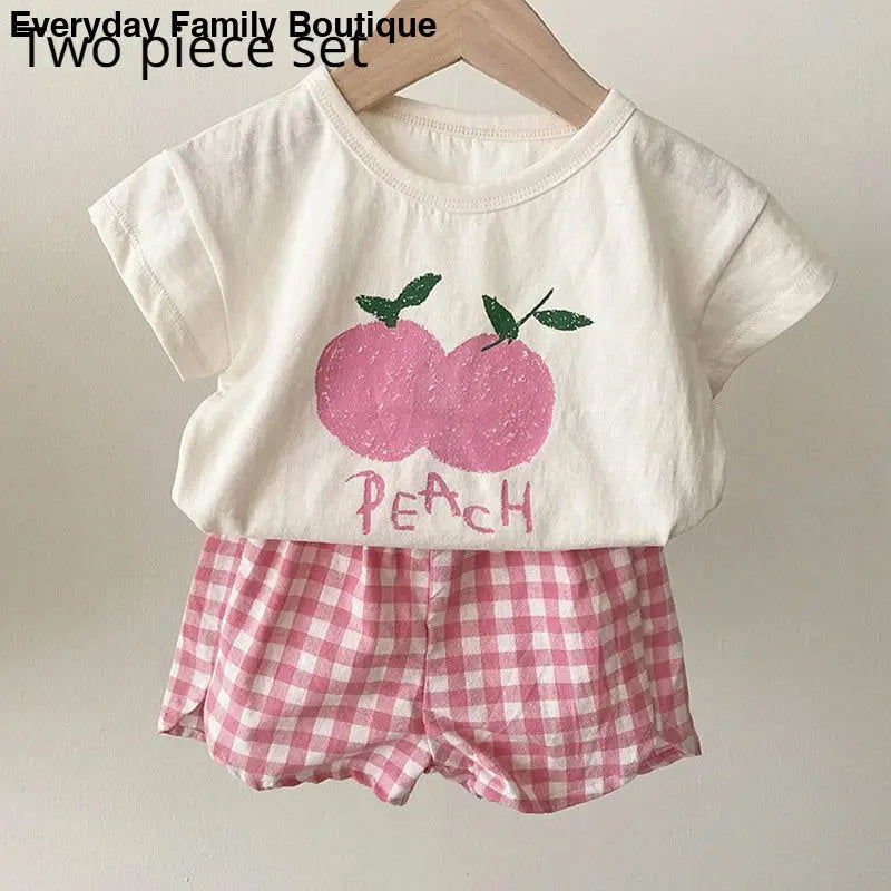 Children’s two-piece outfit with a peach-printed white t-shirt and pink gingham shorts.