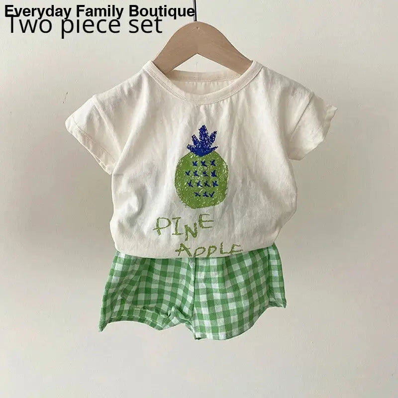 White t-shirt with a pineapple design paired with green gingham shorts.