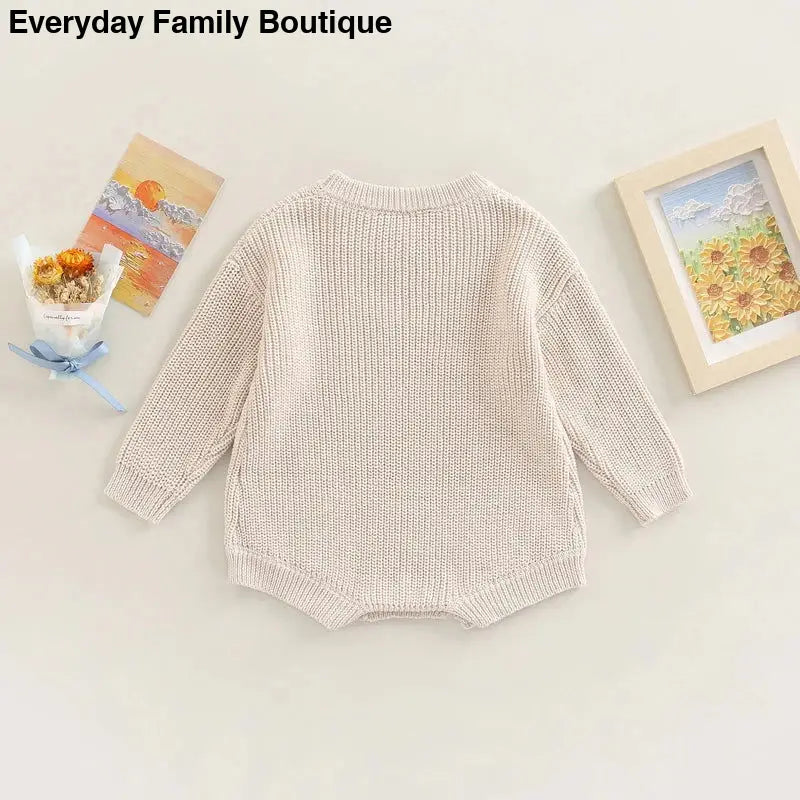 Cream-colored knitted baby romper with long sleeves.