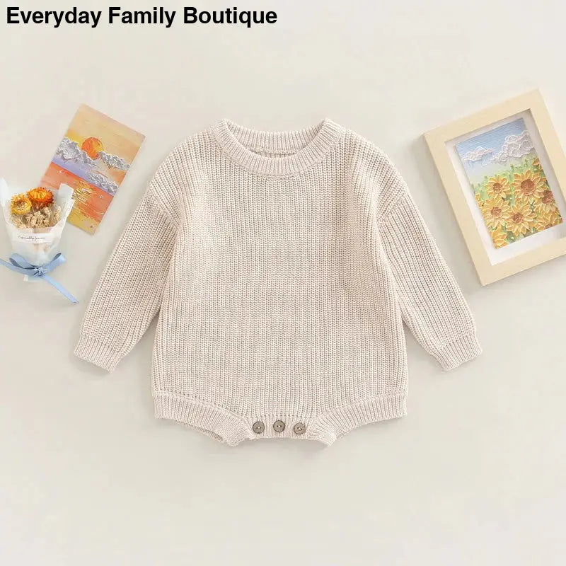 Cream-colored knitted baby romper with button details at the bottom.