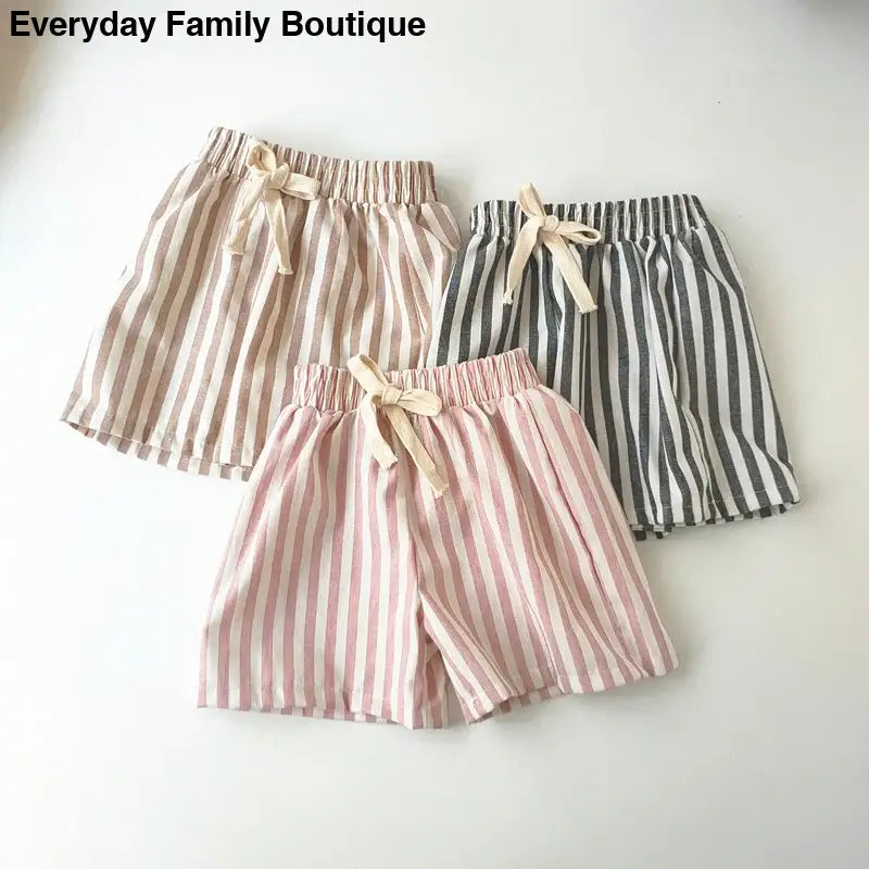 Three pairs of striped cotton shorts with drawstring waists in pink, brown, and gray colors.