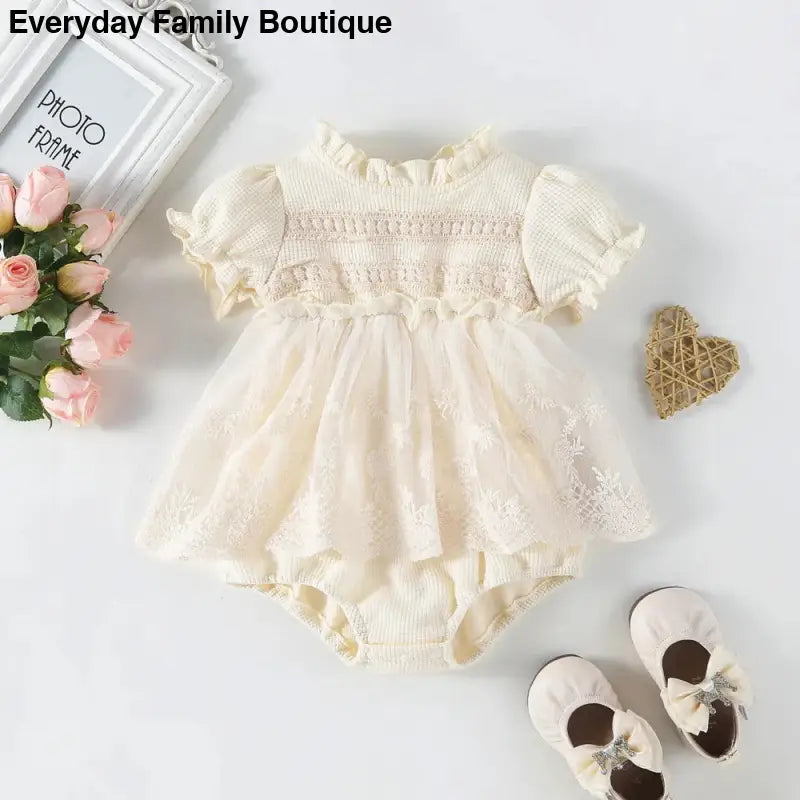 Cream-colored smocked baby romper dress with puff sleeves and delicate lace details.