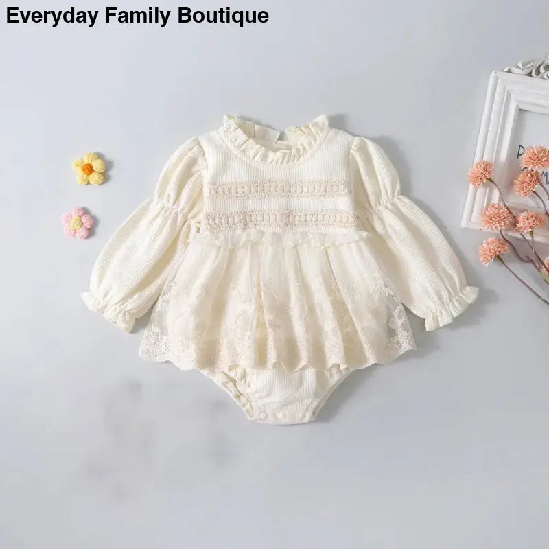 Cream-colored knit baby romper dress with puff sleeves and lace detailing.