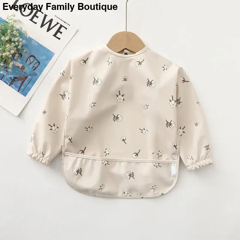 Cream-colored long-sleeve smock with delicate floral print pattern.