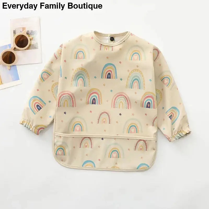 Long-sleeved cream-colored bib with rainbow pattern prints.