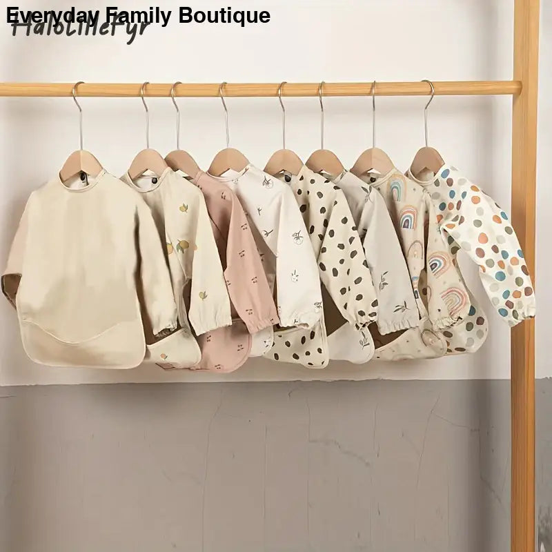 Row of baby clothes hanging on wooden hangers featuring soft pastel colors and various patterns.