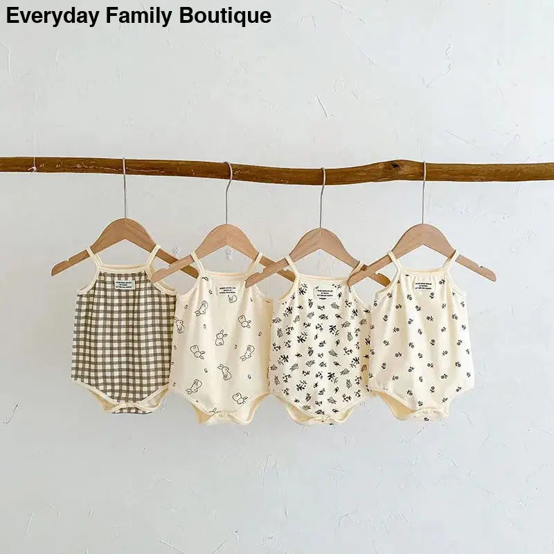 Four baby rompers with different patterns hanging on wooden hangers from a branch.