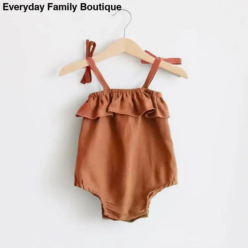 Terracotta-colored baby romper with ruffled top and shoulder ties hanging on a wooden hanger.