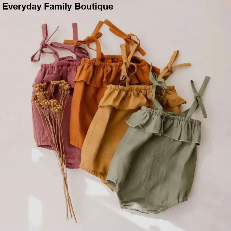 Four baby rompers in earthy tones with shoulder ties and ruffled waistbands.