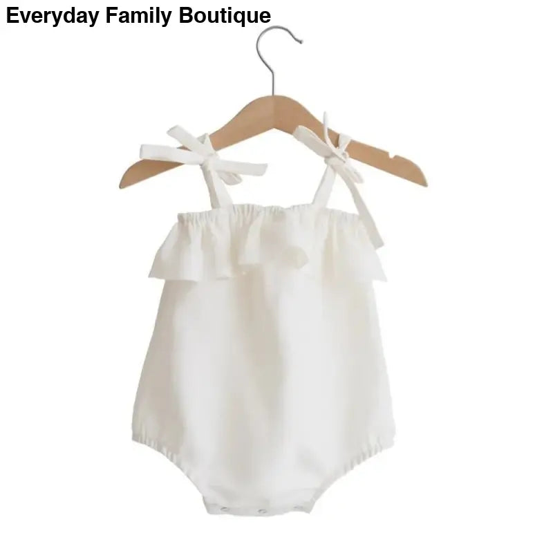 White ruffled baby romper with shoulder ties hanging on a wooden hanger.