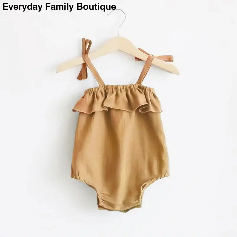 Tan ruffled baby romper with shoulder ties hanging on a wooden hanger.