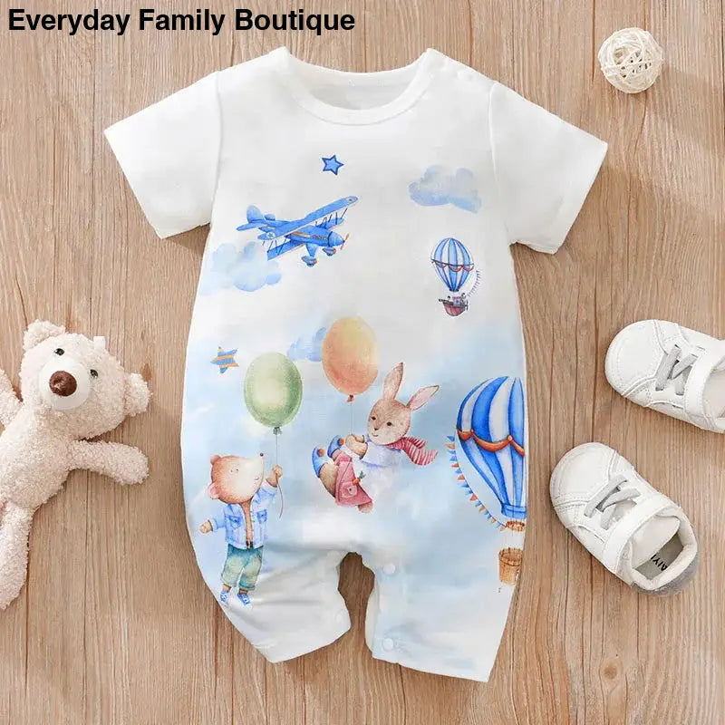 White baby romper with a whimsical print featuring bunnies, balloons, airplanes and hot air balloons.