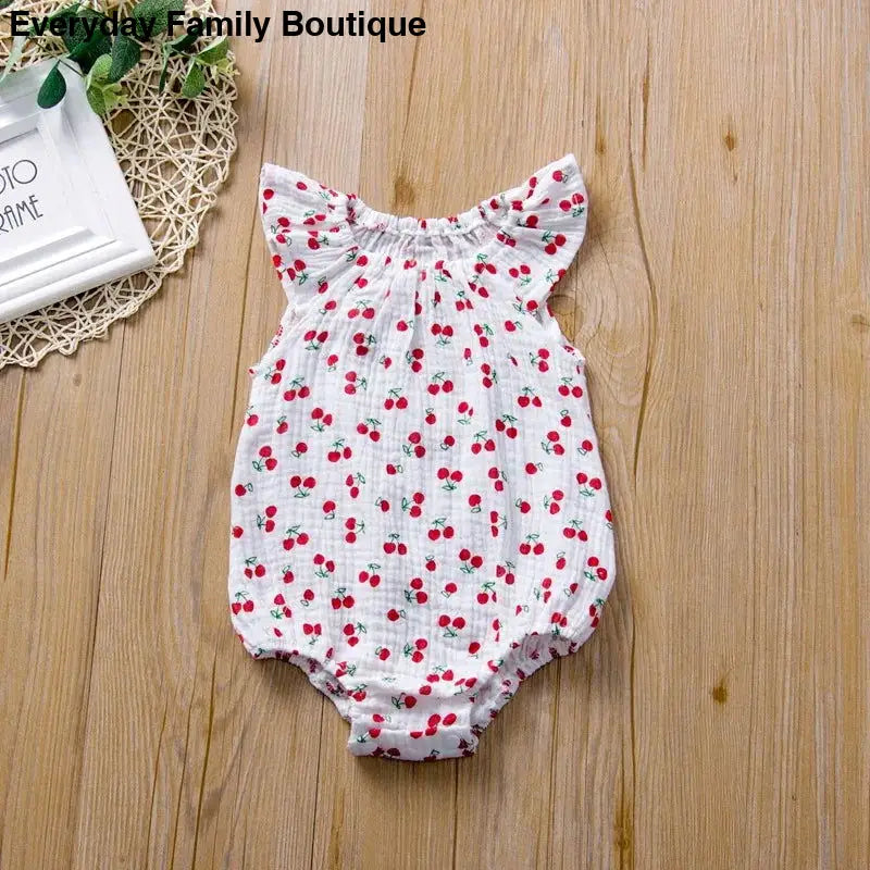 White baby romper with red cherry print and flutter sleeves.