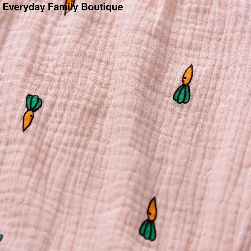 Pink fabric with a repeating pattern of tiny orange and green carrot motifs.