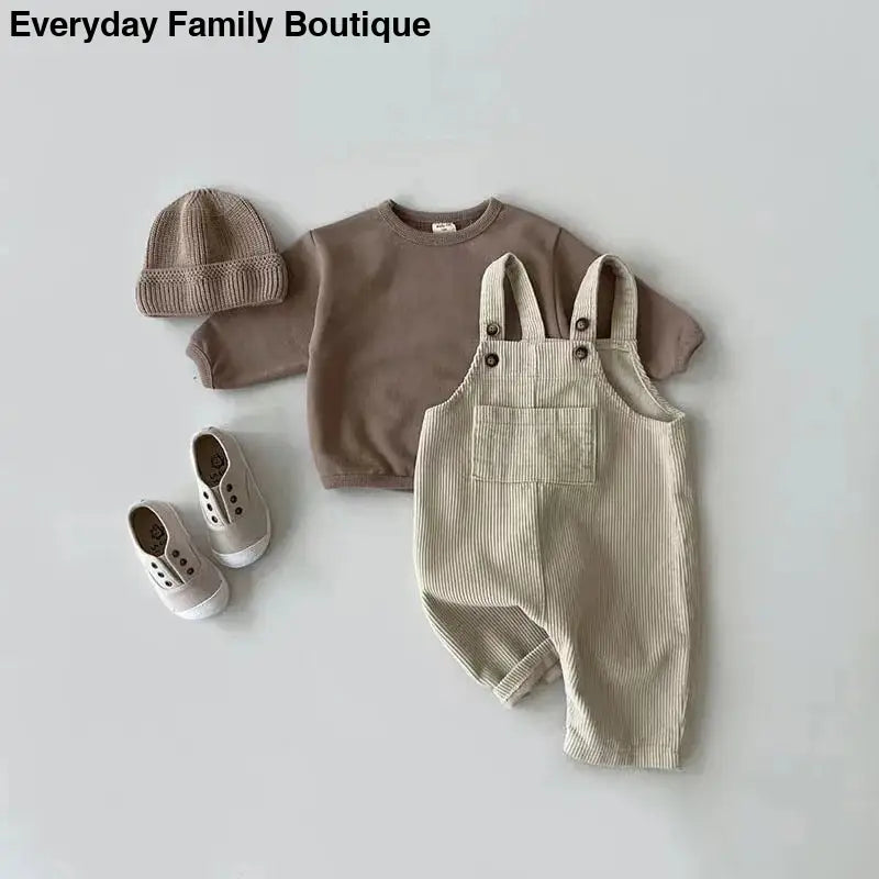 Beige corduroy overalls paired with a brown sweatshirt, knit beanie, and canvas shoes.