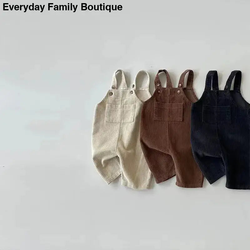 Three pairs of corduroy overalls in cream, brown, and black colors.