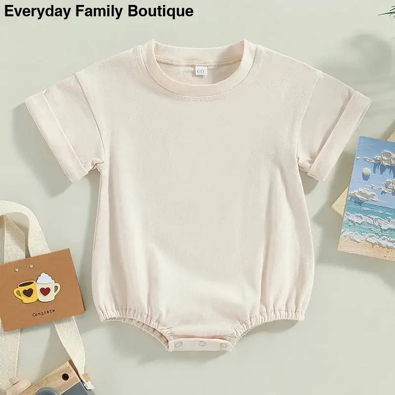 Cream-colored cotton baby romper with short rolled sleeves.