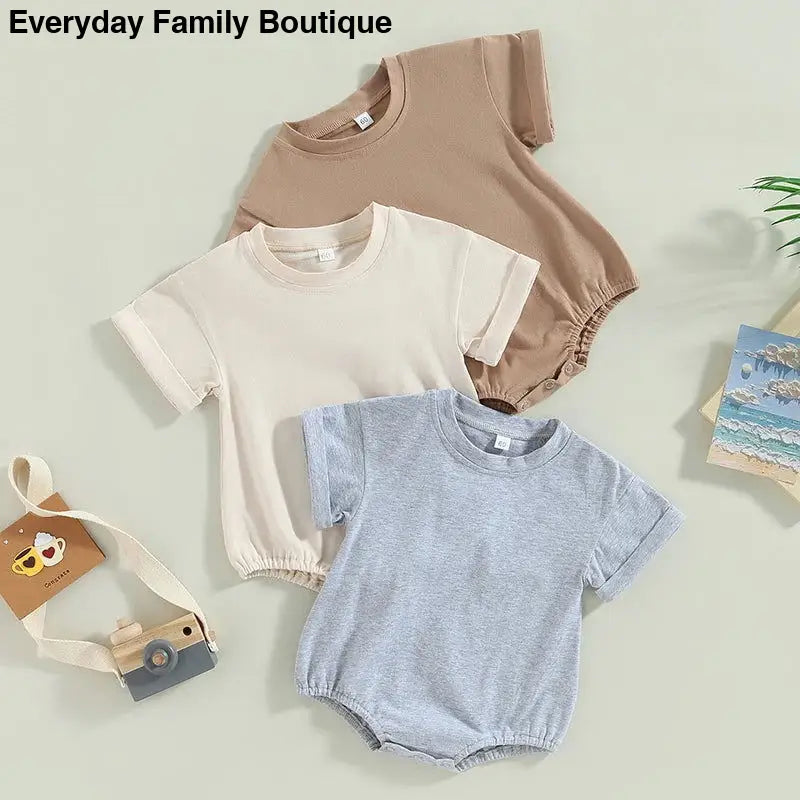 Three baby rompers in beige, cream, and light blue colors with short sleeves and elastic bottoms.