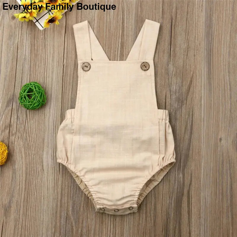 Beige linen baby romper with shoulder straps and buttons.