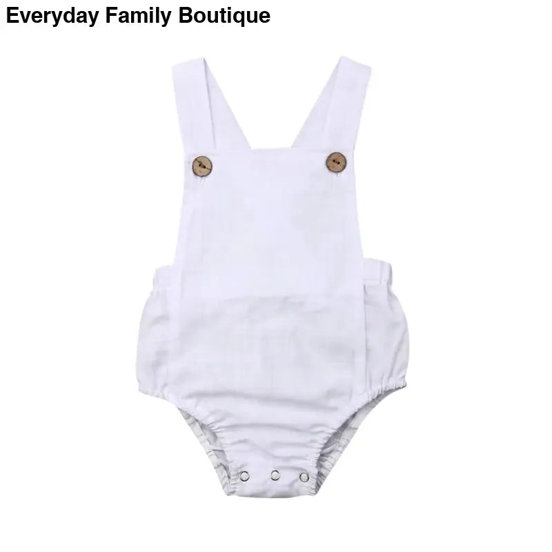 White cotton baby romper with shoulder straps and button closures.