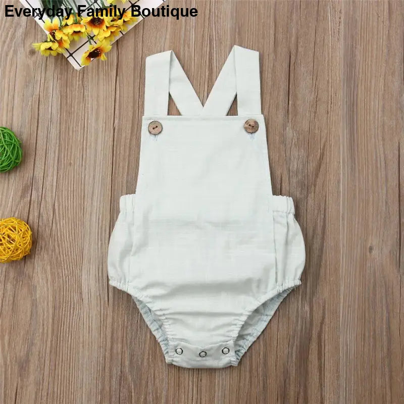 White cotton baby romper with shoulder straps and snap closures.